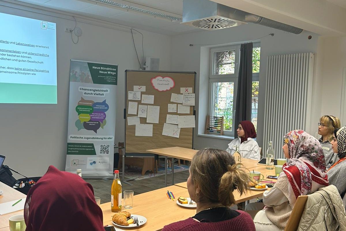 Teilnehmerinnen am Tisch, vorn der Aufsteller „Neue Bündnisse, neue Wege“ und eine Pinnwand zur pluralistischen Gesellschaft
