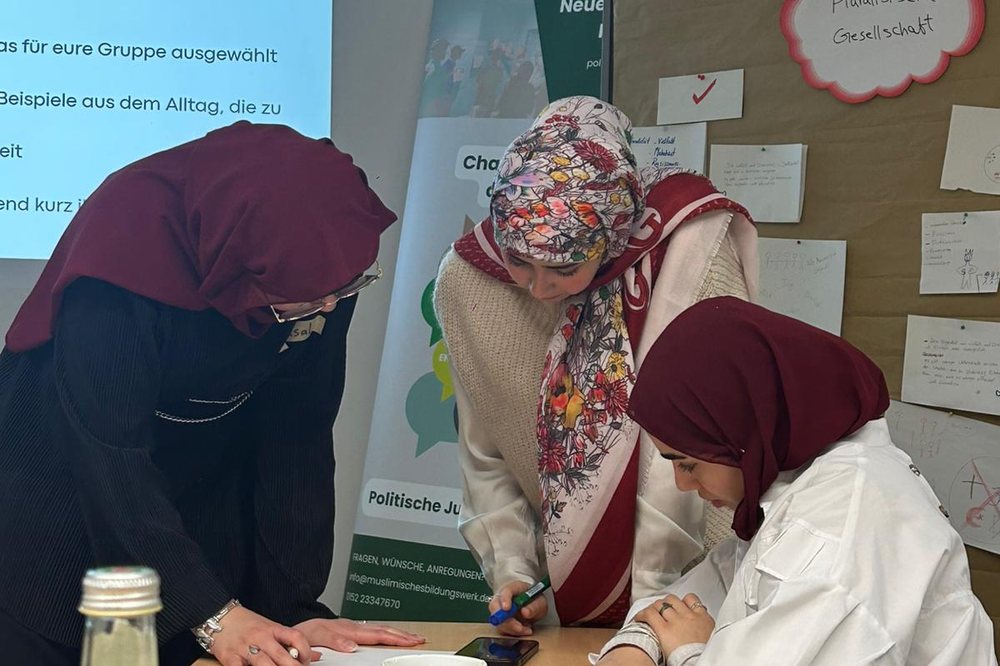 Gruppenarbeit am Tisch vor der Pinnwand „Pluralistische Gesellschaft“