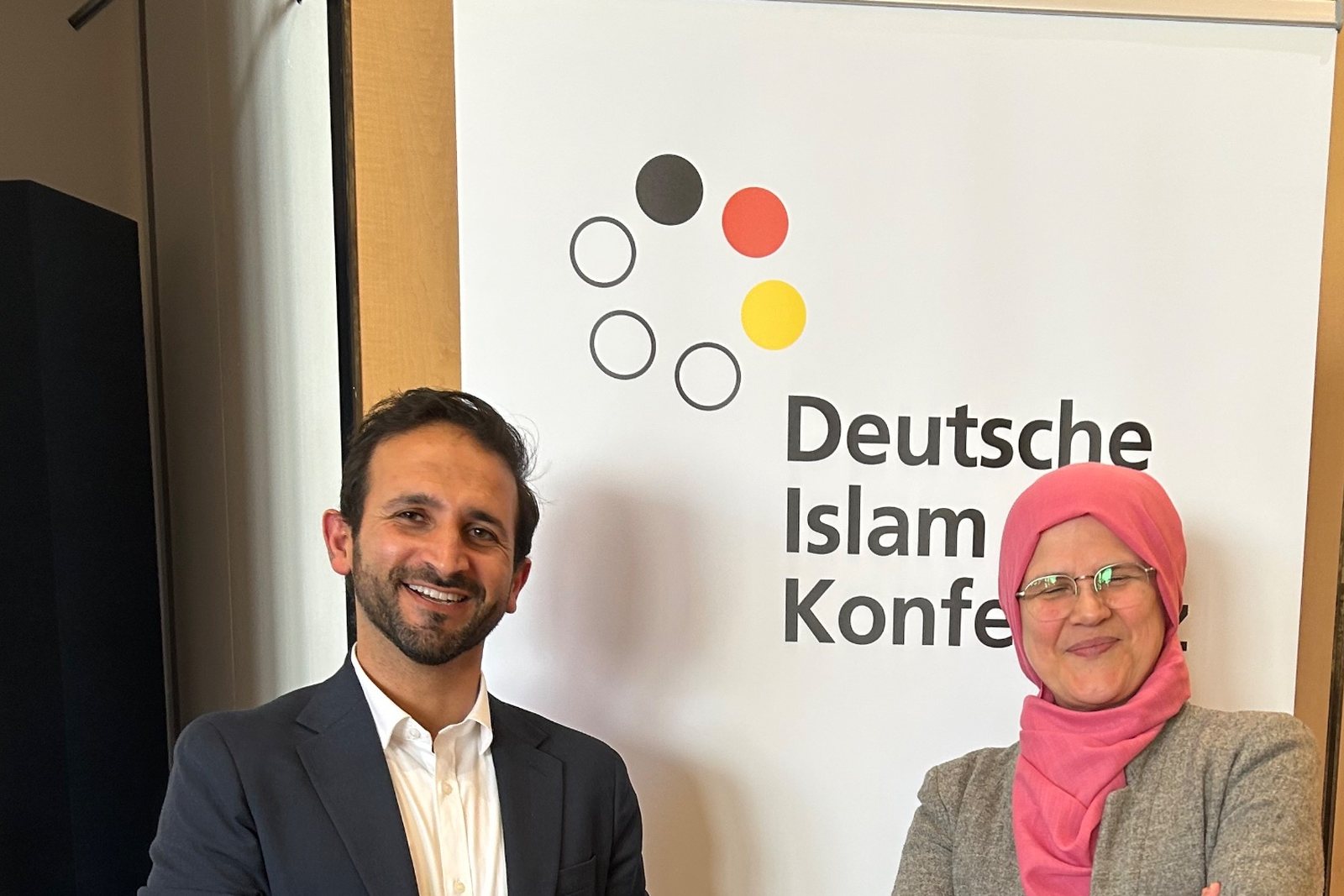 Thaer Issa mit einer Teilnehmerin vor dem Aufsteller der Deutschen Islam Konferenz