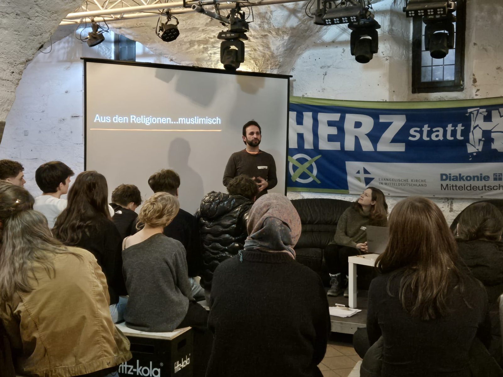 Ein Referent spricht vor der Leinwand mit der Folie „Aus den Religionen … muslimisch“ zu den Jugendlichen