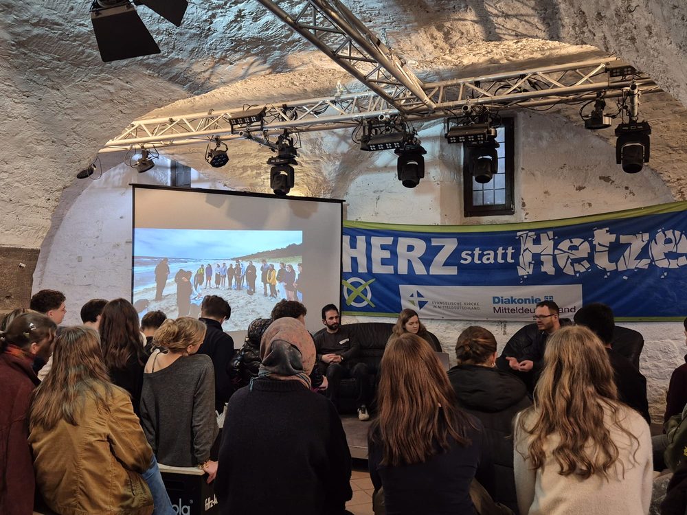 Gesprächsrunde mit drei Gästen auf dem Sofa vor dem Banner „Herz statt Hetze“
